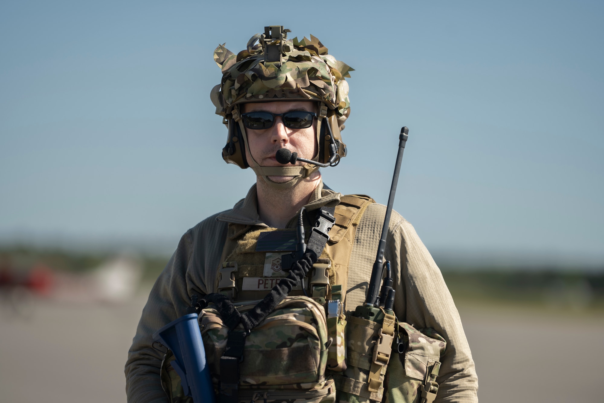 A photo of a person in battle rattle, holding a dummy gun, posing for a photo.