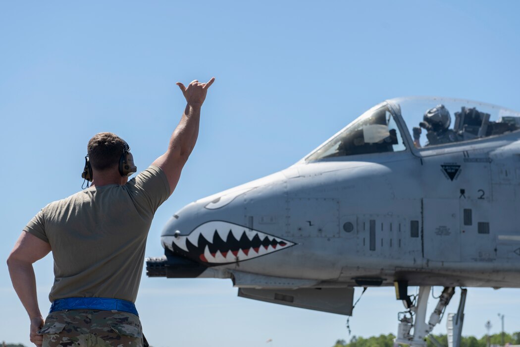 A person to the left of the photo presenting a "hang loose" to a pilot preparing for take off.