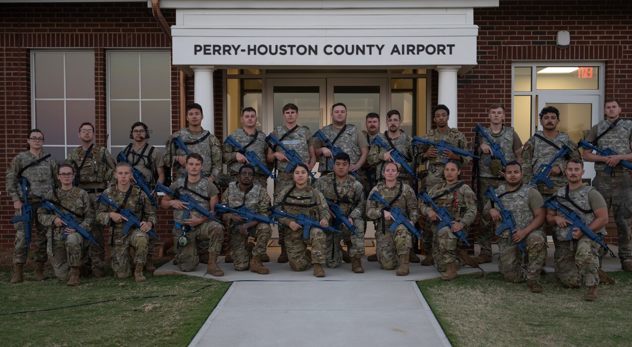 A group photo of 24 people posing in front of an airport sign.