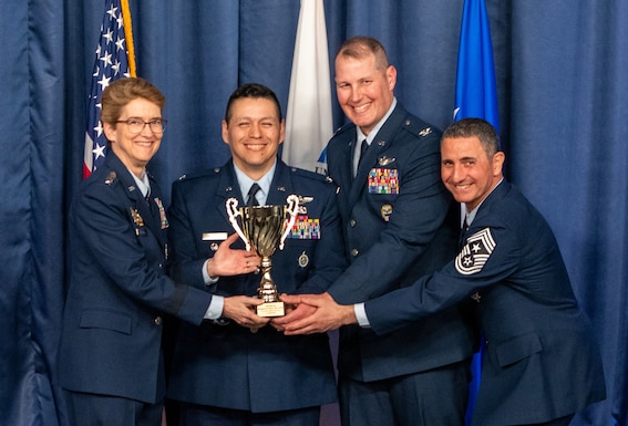 Four people in Air Force dress uniforms hold a trophy