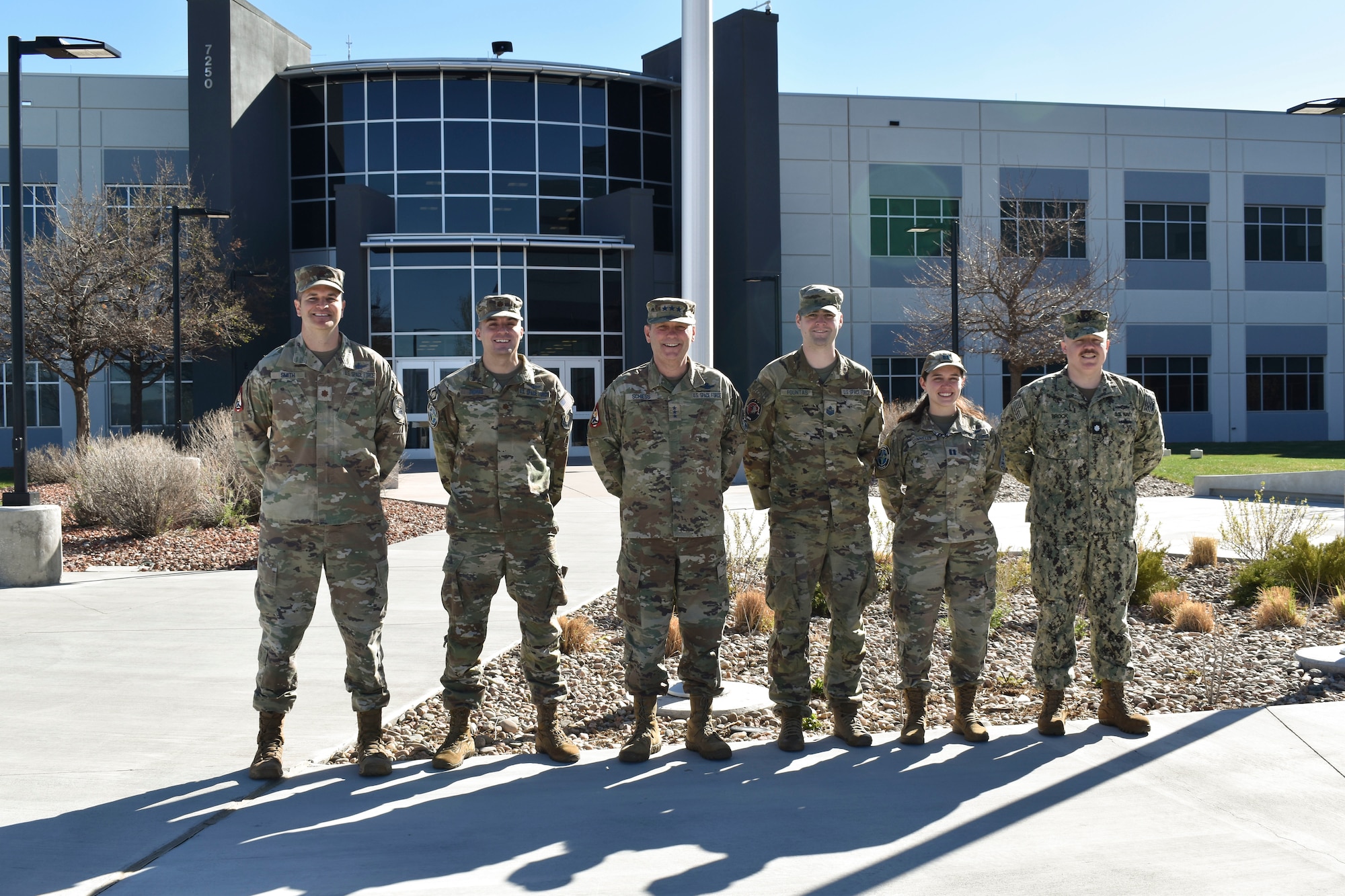 Military members in uniform posing for a group photo outside of the building