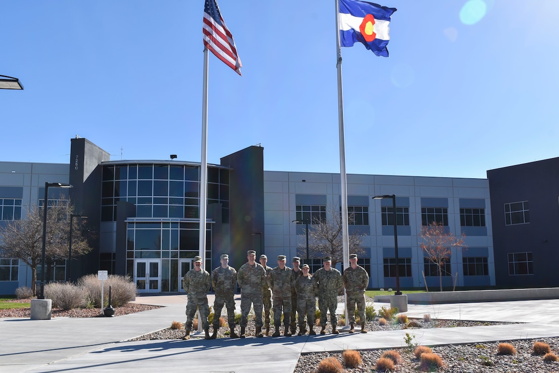 Military members in uniform posing for a group photo outside of the building