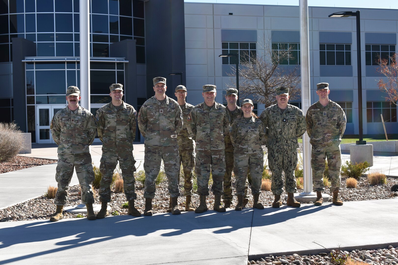 Military members in uniform posing for a group photo outside of the building