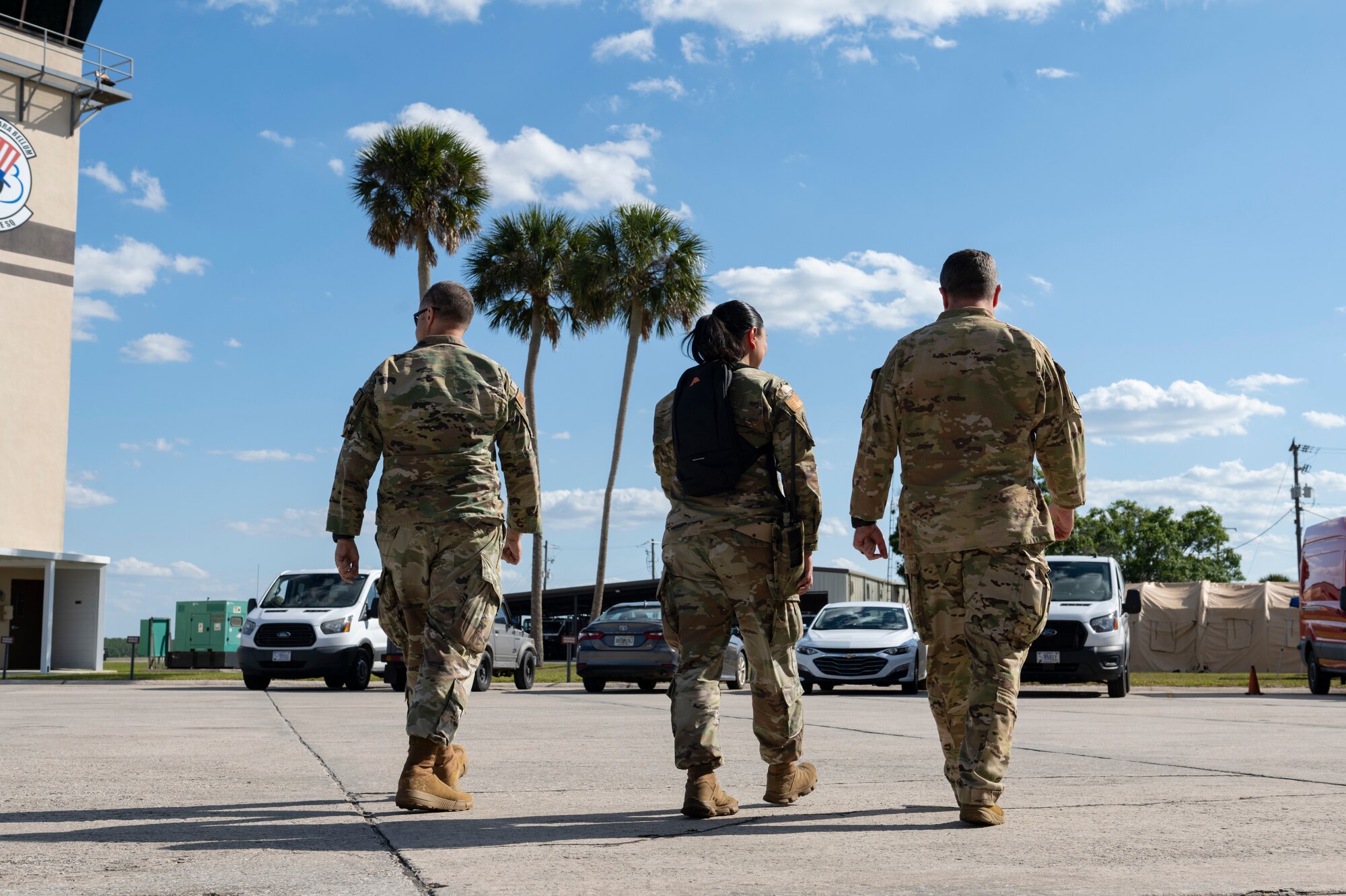 Three people walking away from the camera with the sky and palm trees in the background.