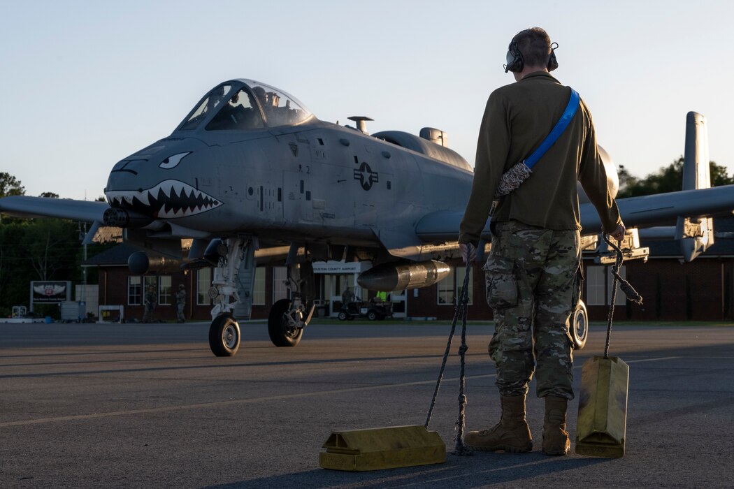 A photo of someone standing in front of an A-10C, holding chocks.