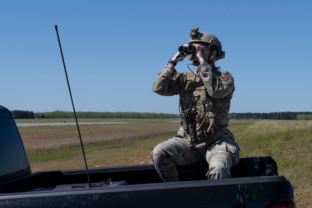 A girl sitting on the back of a truck bed looking through binoculars.