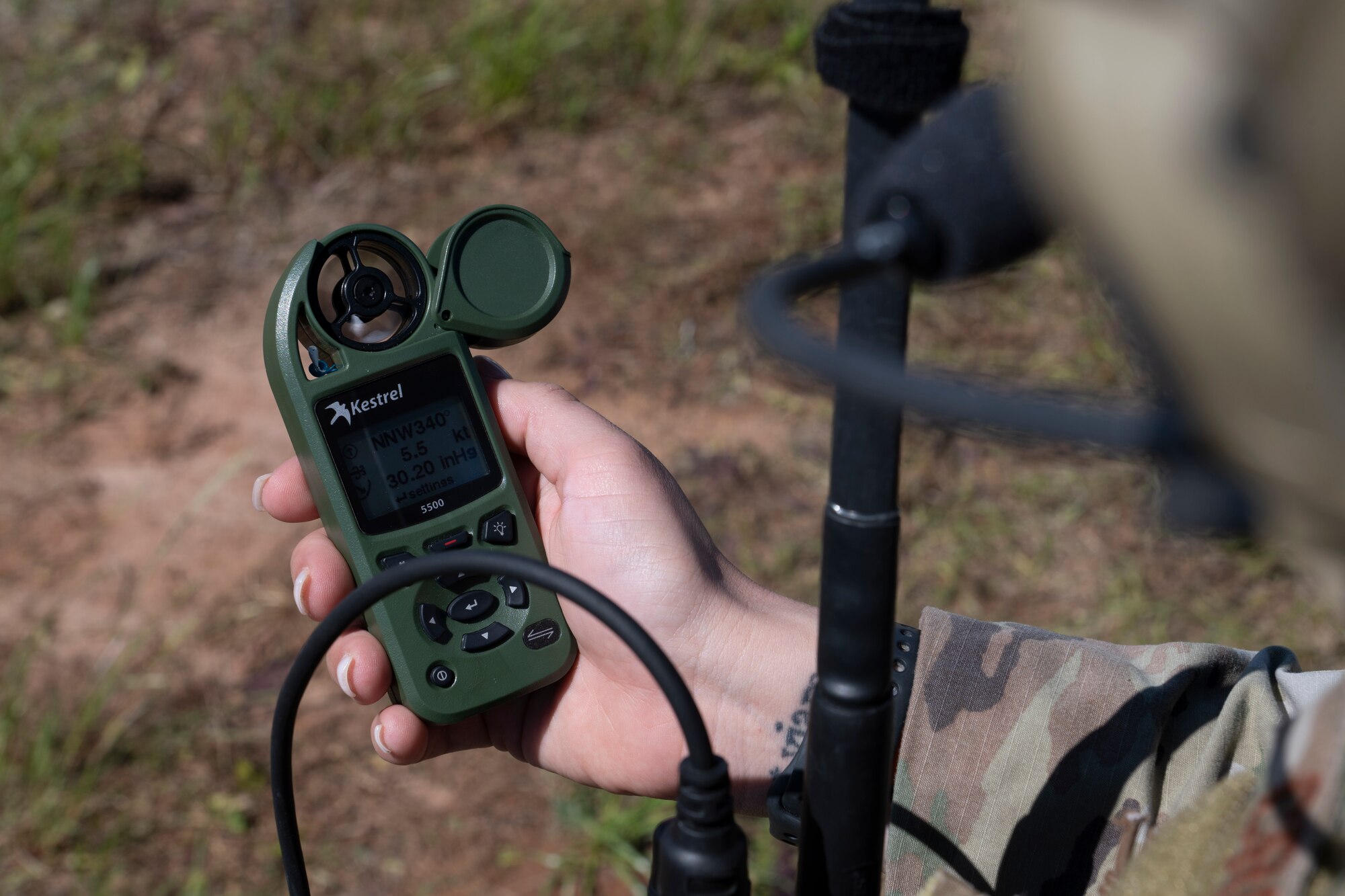 A photo of a person holding a weather device. The photo was taken over their left shoulder.