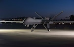 An MQ-9 sits on the airfield at dusk.