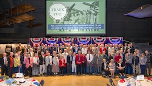 Image of a group of almost 400 volunteers standing in front of a screen in the museum's 2nd hangar with the words "thank you" on the screen.