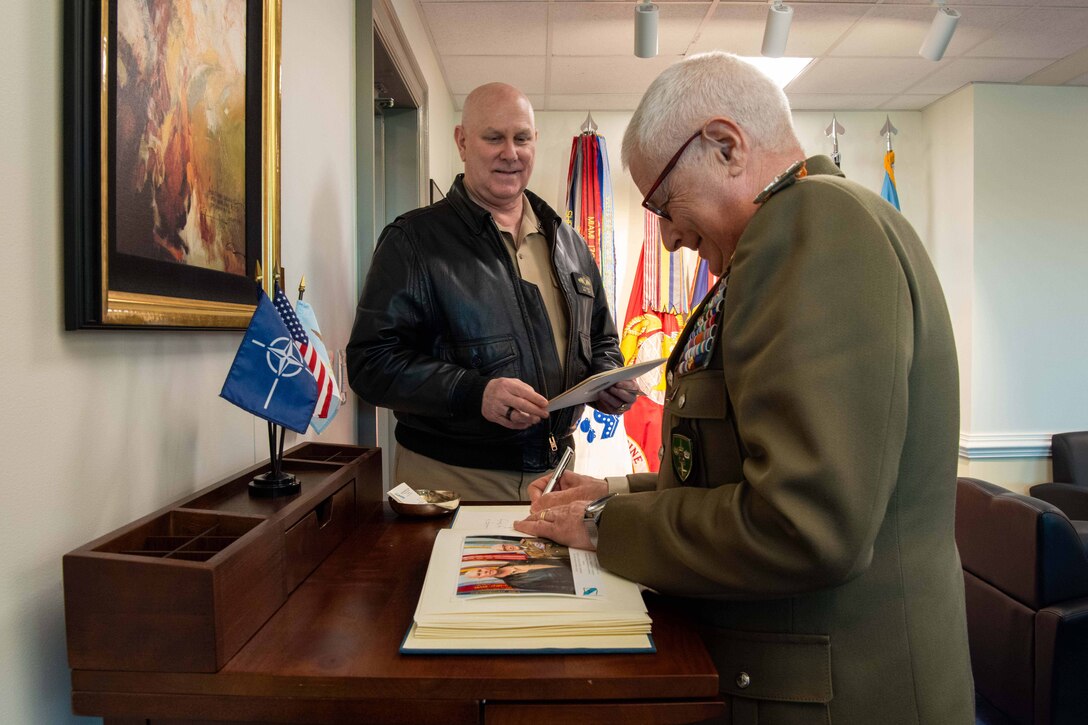 Navy Adm. Christopher W. Grady, vice chairman of the Joint Chiefs of Staff, watches another leader sign a guest book.