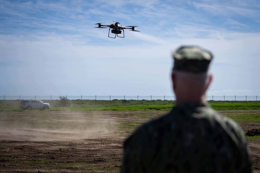 Navy Adm. Christopher W. Grady, vice chairman of the Joint Chiefs of Staff, watches a drone in flight against a partly cloudy sky.