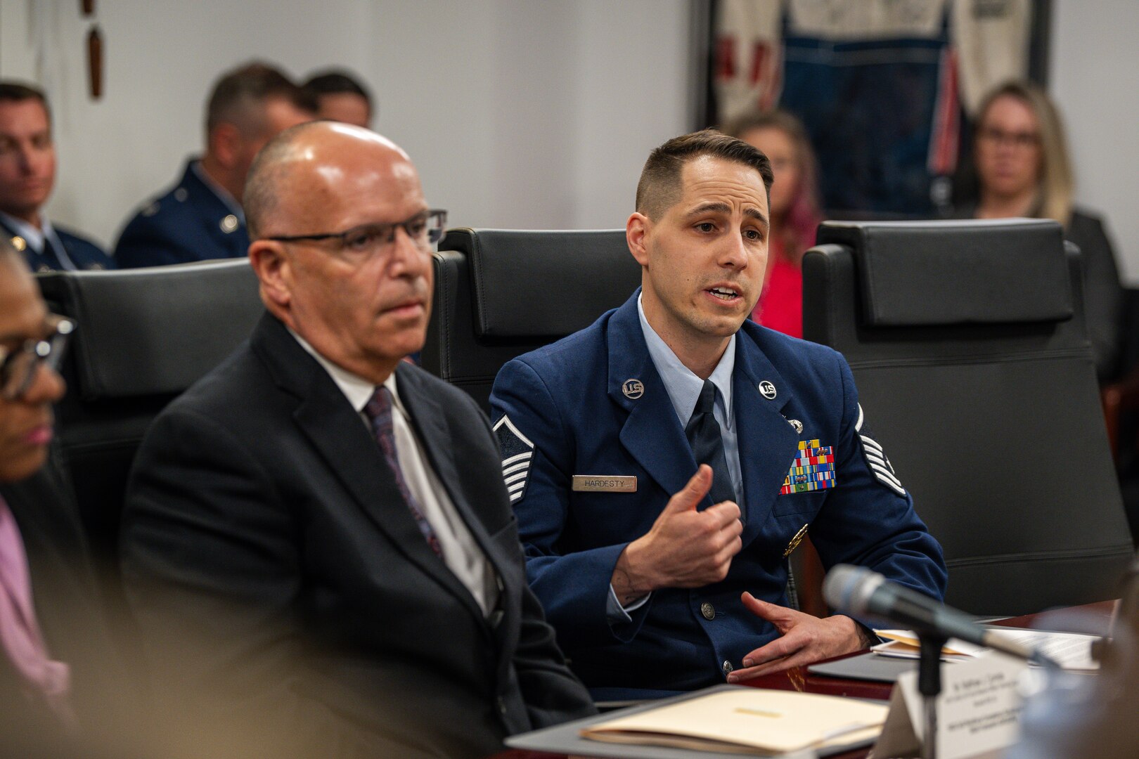 An airman speaks into a microphone surrounded by others.