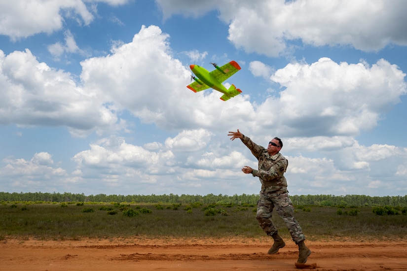 An airman runs as he throws a small aircraft into the air in a large field.