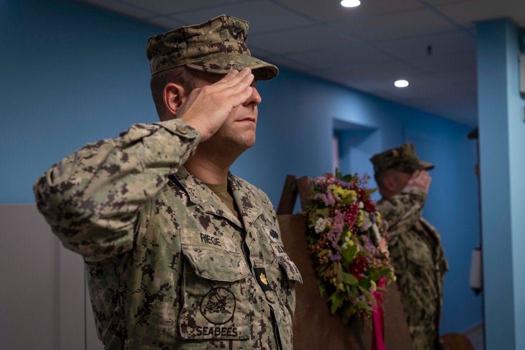 From left to right, Lt. Cmdr. Matthew Riege, public works officer, Naval support Activity Souda Bay, and Chief Builder Earl Doan, assigned to Naval Facilities Engineering Systems Command Europe Africa Central, render salutes during a memorial service for Naval Mobile Construction Battalion (NMCB) 14 in The Anchor on May 2, 2024.