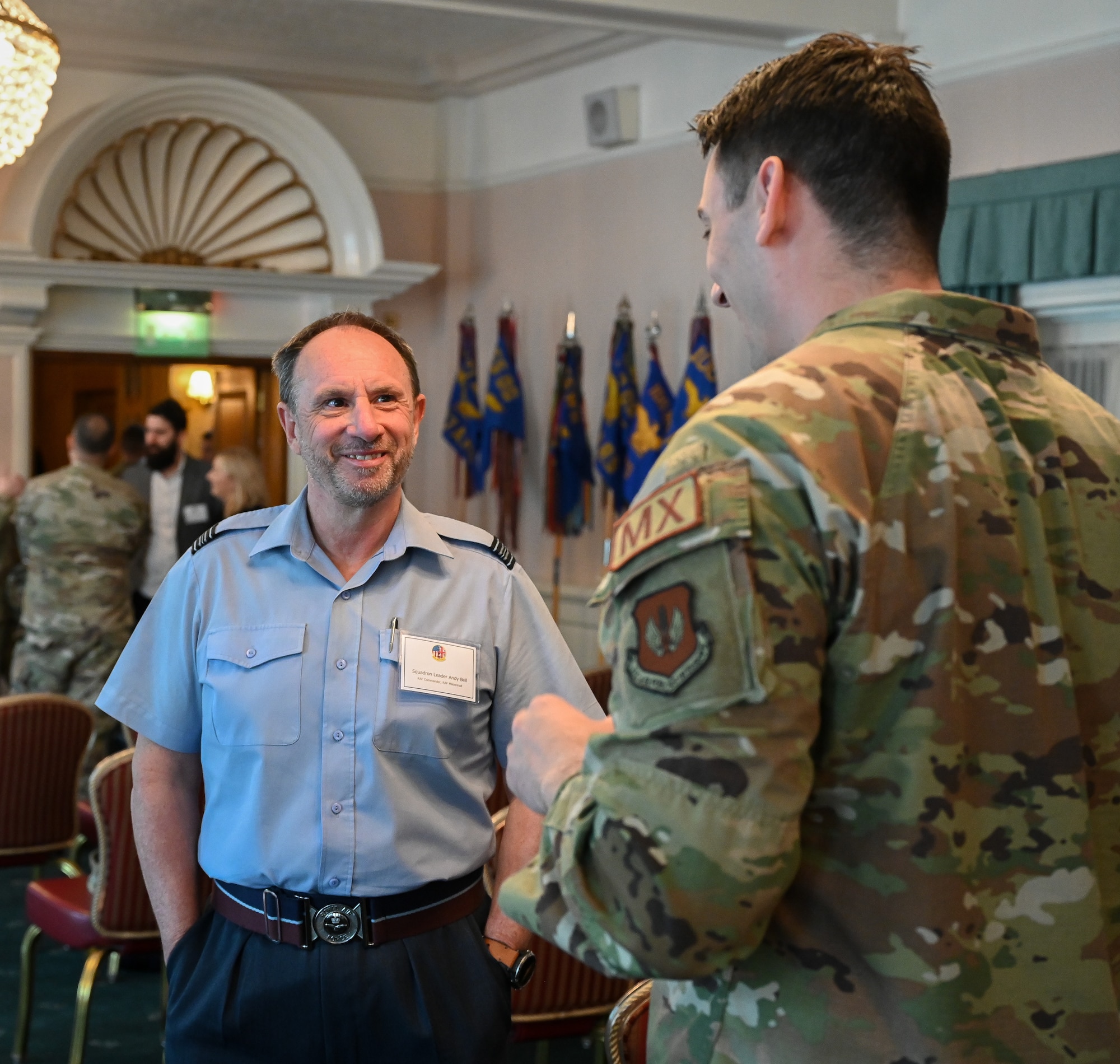 Royal Air Force Sqn Ldr Andy Bell, left, RAF Mildenhall commander, speaks with U.S. Air Force Capt. Nicholas Sauer, 100th Maintenance Group executive officer, while taking a refreshment break during the honorary commander induction ceremony at RAF Mildenhall, England, April 24, 2024.