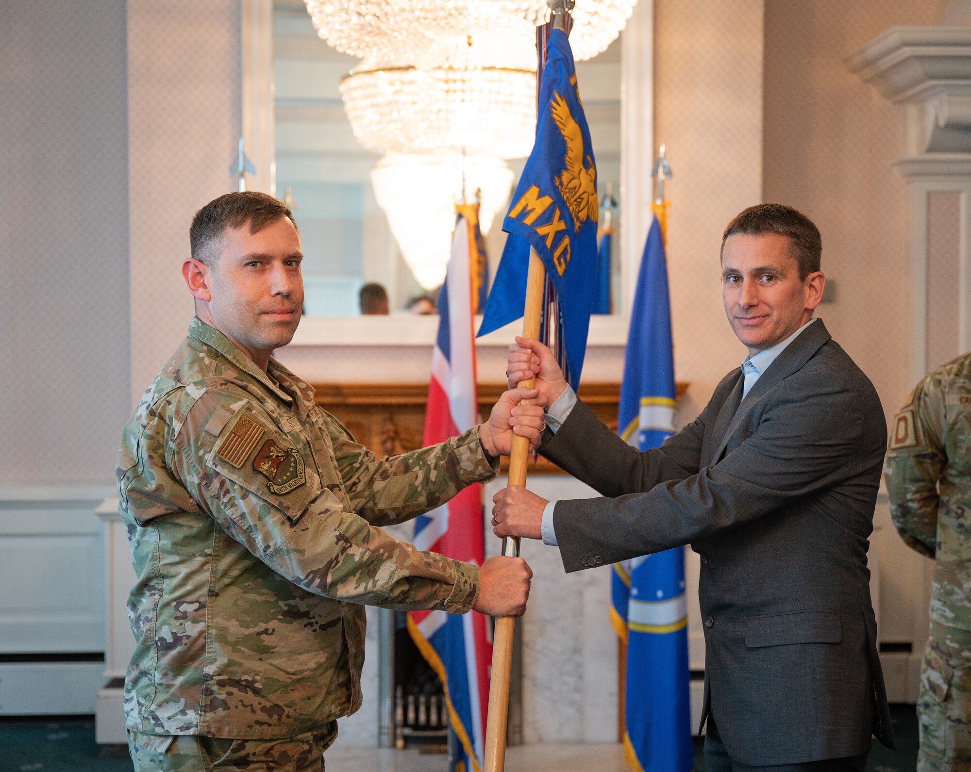U.S. Air Force Lt. Col. Charles Schulz, left, 100th Maintenance Group deputy commander, passes the 100th MXG guidon to Gary Jefferson, West Suffolk College group deputy principal, during the honorary commanders’ induction ceremony at Royal Air Force Mildenhall, England, April 24, 2024.