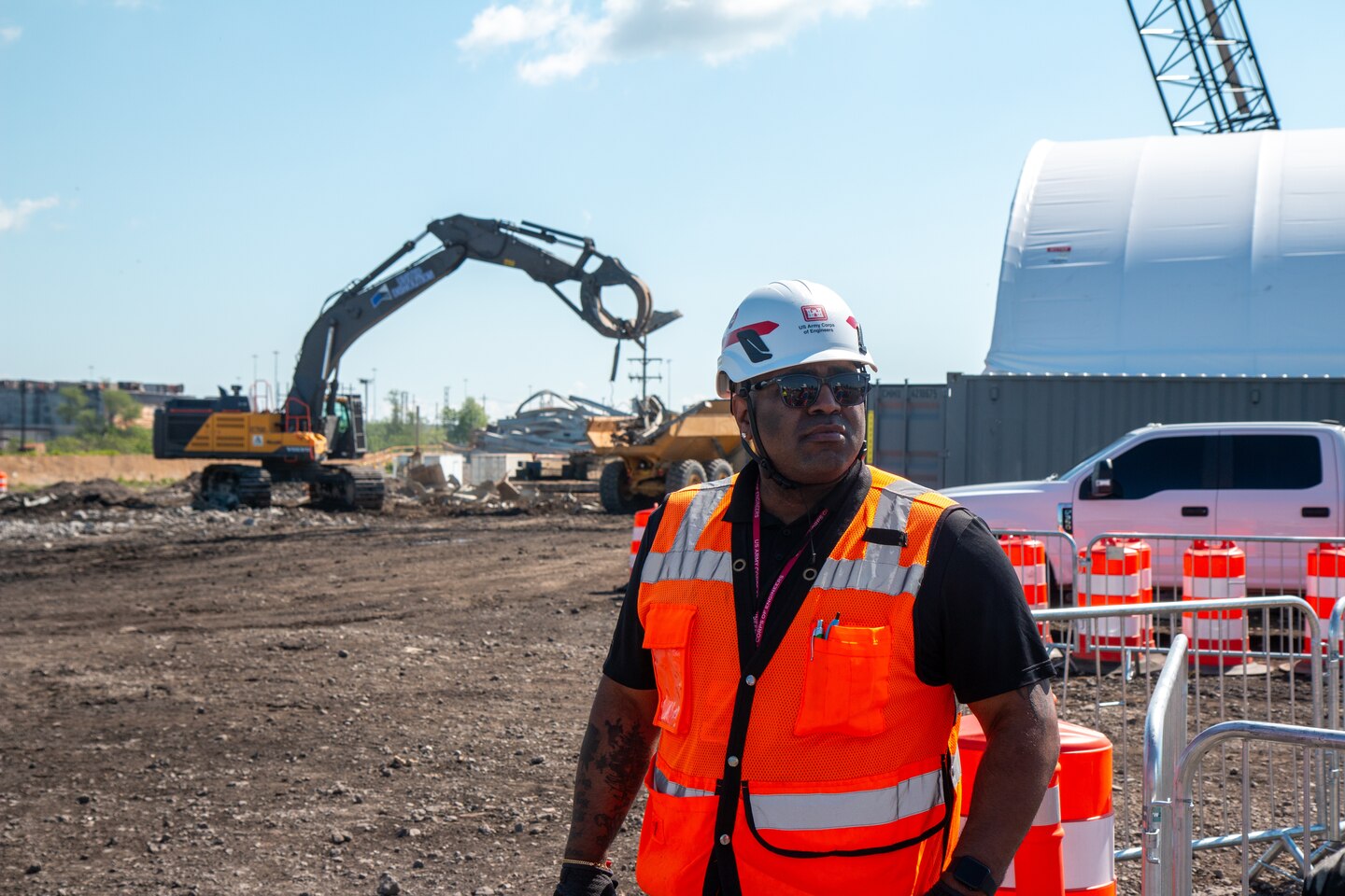 A man in a hardhat and safety vest views a salvage site.
