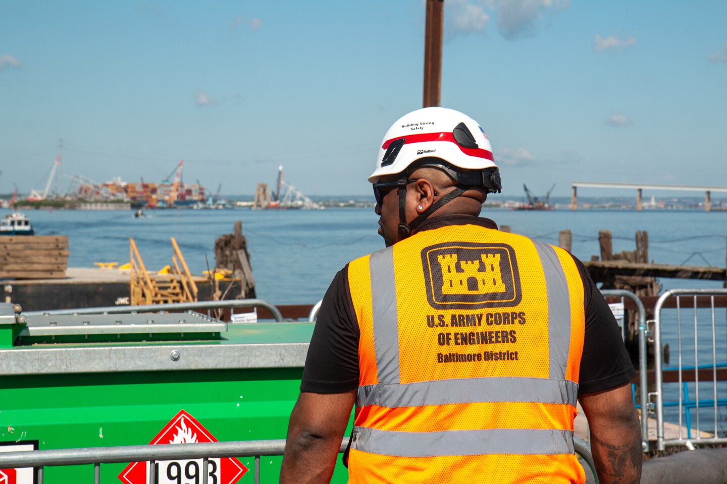 A man in a hardhat and safety vest views a salvage site.