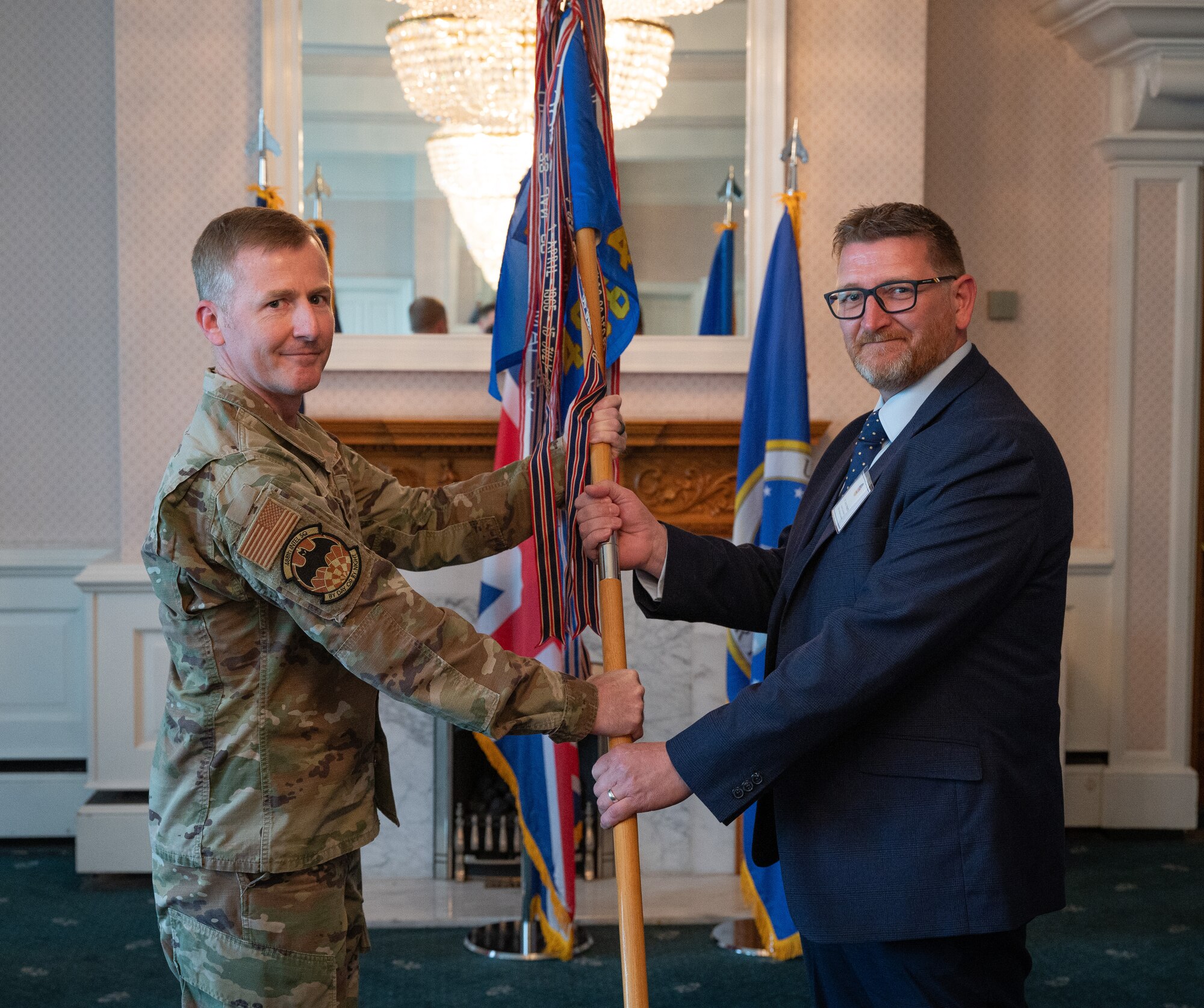 U.S. Air Force Lt. Col. Bradley Higby, left, 488th Intelligence Squadron commander, passes the 488th IS guidon to Aaron Kesketh, head of the National Trading Standards Intelligence Team, during the Honorary Commanders’ induction ceremony at Royal Air Force Mildenhall, England, April 24, 2024.