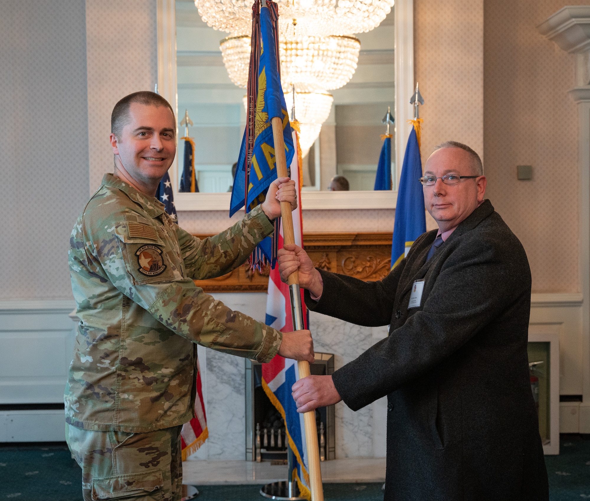 U.S. Air Force Maj. Scott Conrad, left, 727th Air Mobility Squadron commander, passes the 727th AMS guidon to James Clarey, 453nd Bombardment Group Museum curator, during the honorary commanders’ induction ceremony at Royal Air Force Mildenhall, England, April 24, 2024.