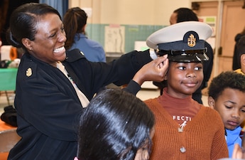 LSC Krystal Belcher, from NAVSUP FLC Norfolk, places a combination cover on a student's head during a career fair at an elementary school in Norfolk.