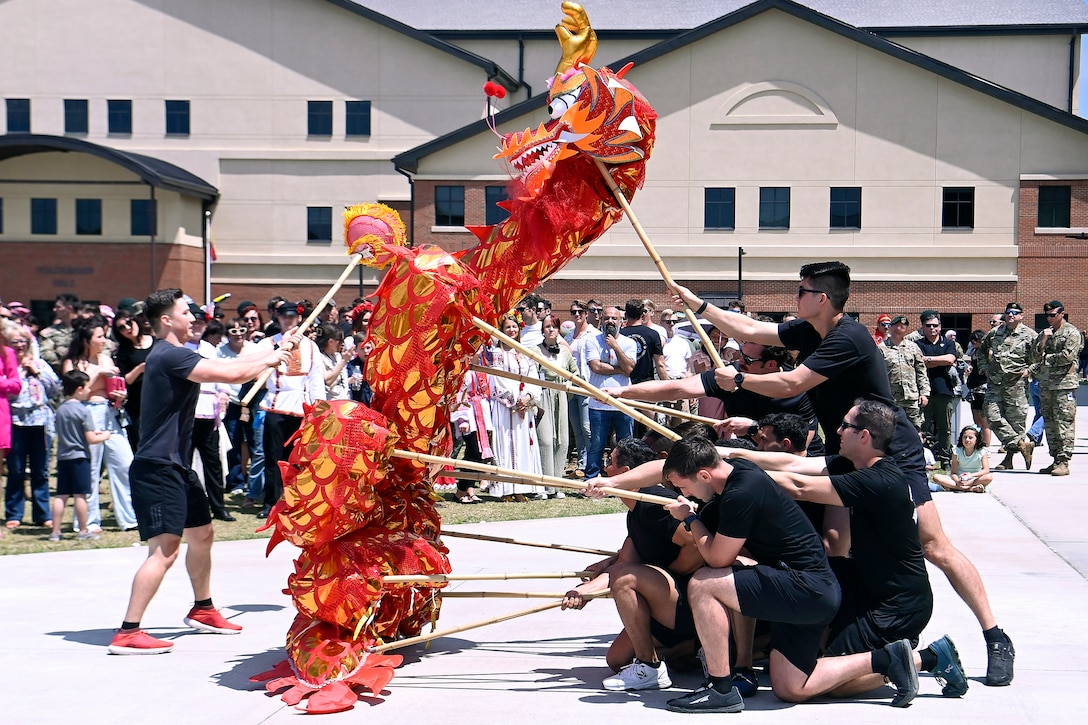 Soldiers hold sticks to move around a paper dragon in front of an audience outside of a building.
