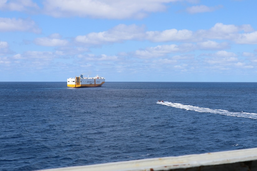 A small boat heads across the water to a larger ship.