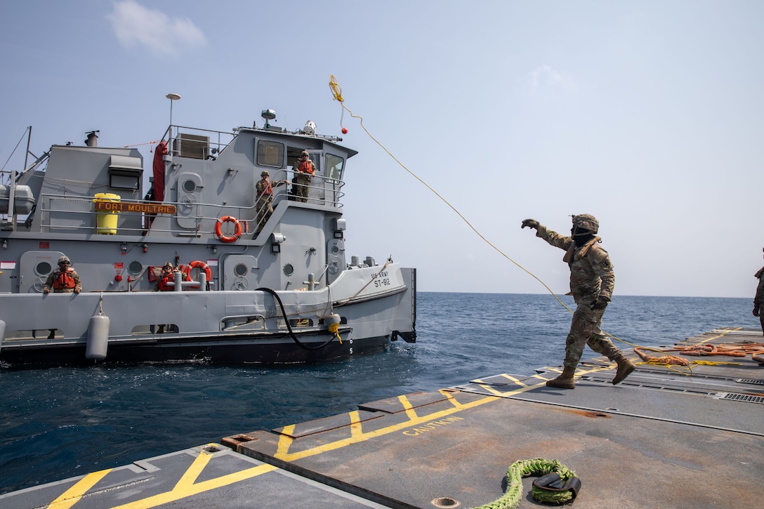 A U.S. Army Soldier assigned to the 7th Transportation Brigade (Expeditionary) tosses a line to an Army tug vessel from the Roll-On, Roll-Off Distribution Facility (RRDF), or floating pier, off the shore of Gaza in support of Operation Neptune Solace, May 1, 2024. The temporary pier will assist the United States Agency for International Development in the delivery of humanitarian aid to the people of Gaza, which will increase the quantity and flow of humanitarian aid, including food, water, medicine, and temporary shelters.