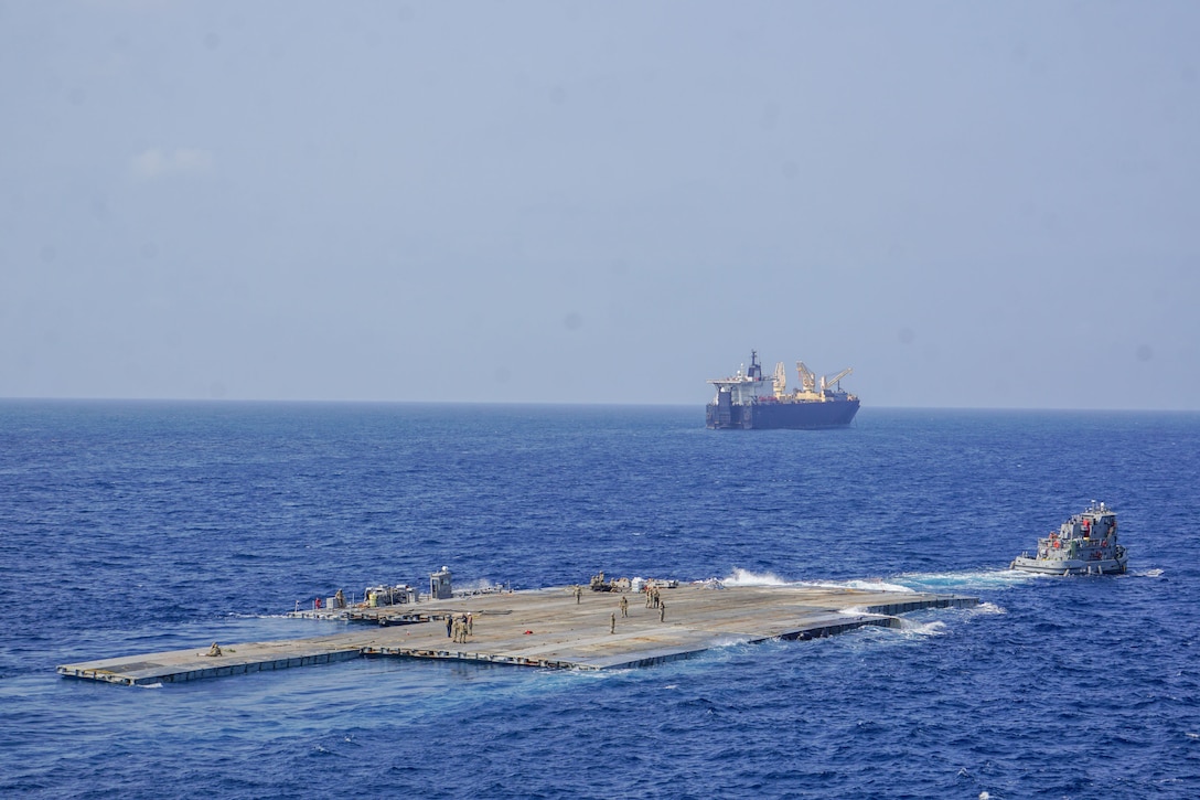 The Roll-On, Roll-Off Distribution Facility, or floating pier, is pulled by an Army tug boat from the 7th Transportation Brigade (Expeditionary) off the shore of Gaza during Operation Neptune Solace, May 1, 2024. The temporary pier will assist the United States Agency for International Development in the delivery of humanitarian aid to the people of Gaza, which will increase the quantity and flow of humanitarian aid, including food, water, medicine, and temporary shelters.