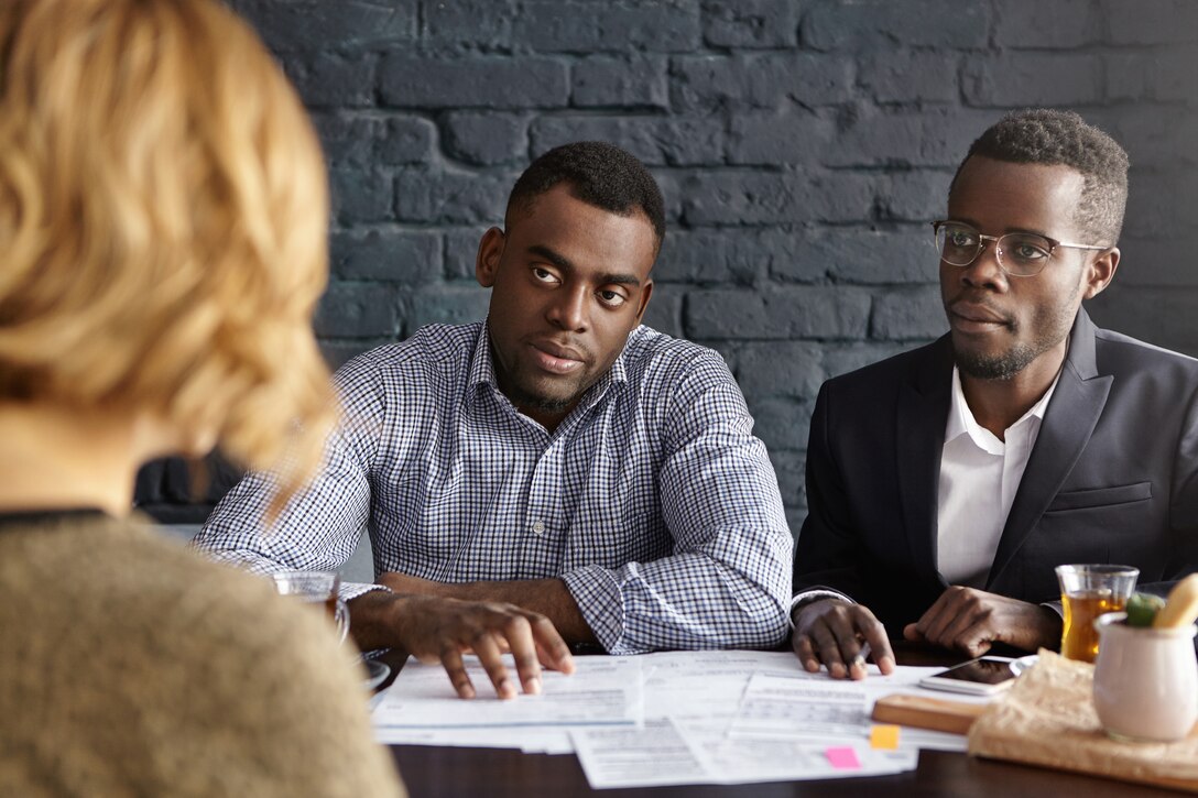 Unrecognizable Caucasian female being interviewed by doubtful future boss and HR director, who sitting at desk with papers in front of her, asking questions about job experience and personal qualities