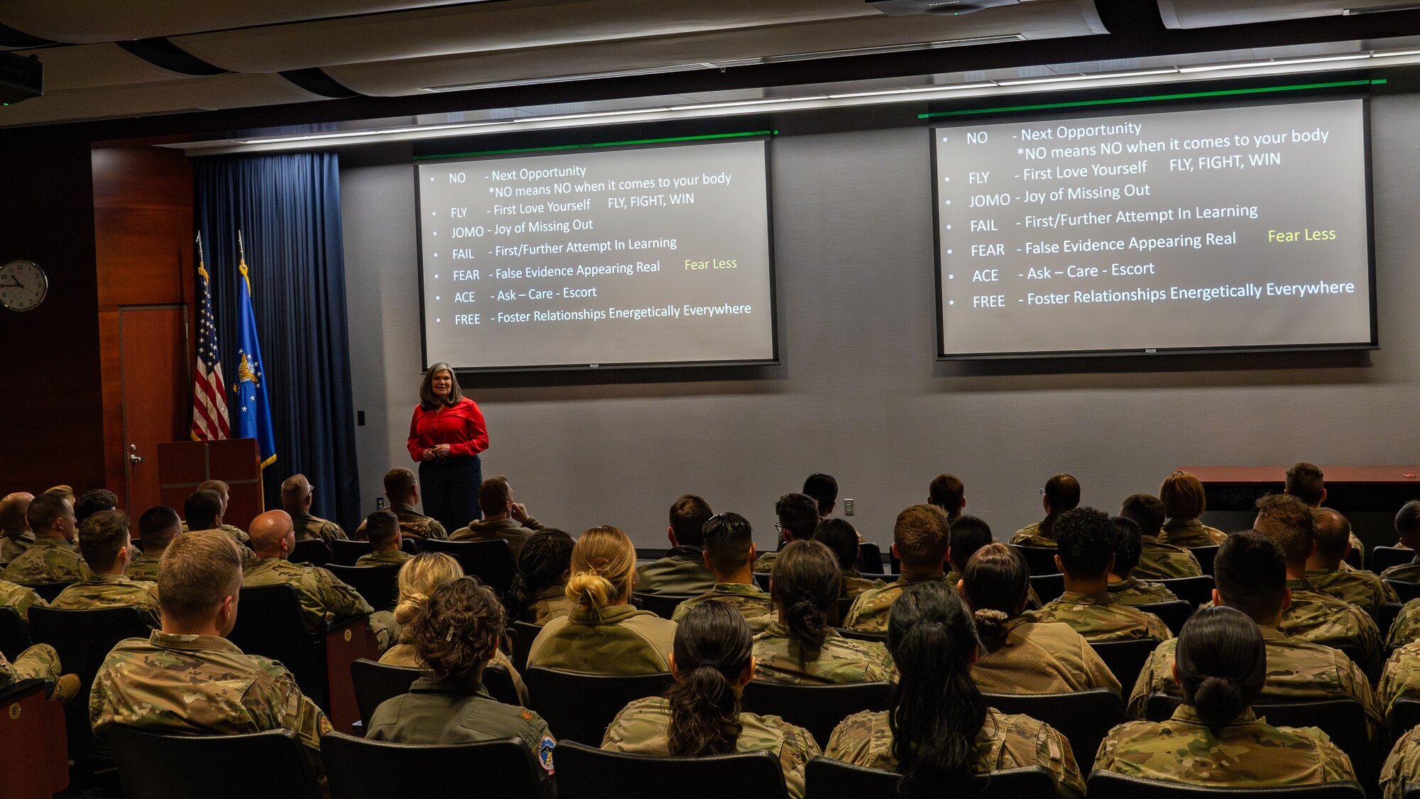 A woman speaks in front of a crowd of uniformed military personnel.