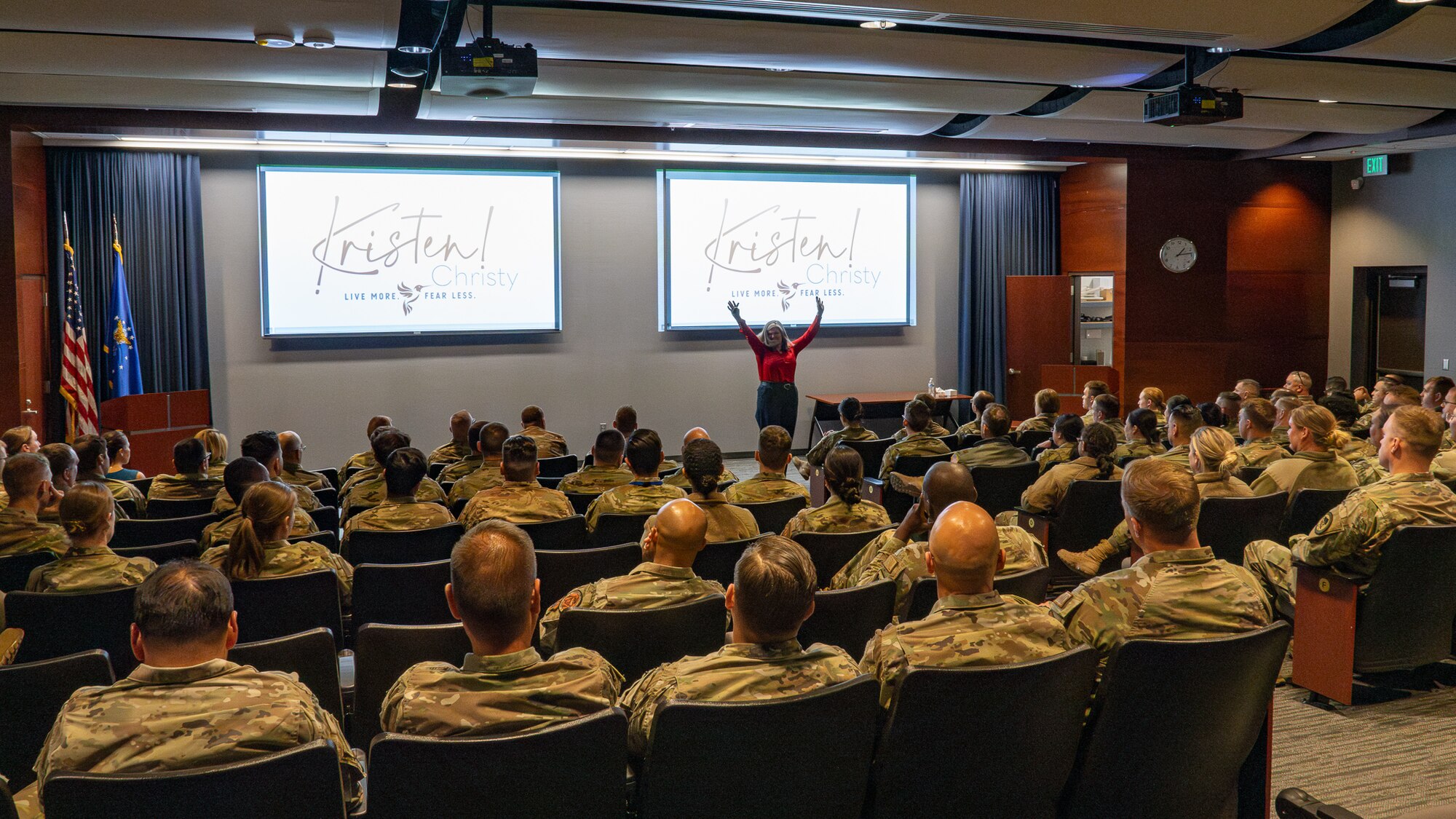 A woman speaks in front of a crowd of uniformed military personnel.