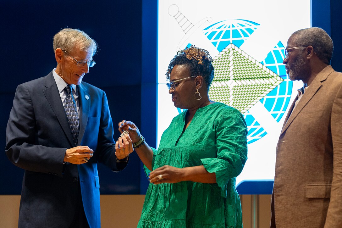 Robert Speer, former acting Secretary of the Army and Assistant Secretary of the Army for Financial Management and Comptroller, gives a Finance and Comptroller Hall of Fame regimental lapel pin to Renee Warren-Morrissette as she prepares to pin it on her husband, retired Command Sgt. Maj. Paul L. Morrissette, during a hall of fame induction ceremony at the Soldier Support Institute on Fort Jackson, South Carolina, April 26, 2024. Morrissette, a former Finance Corps regimental sergeant major, was made the third inductee of the hall of fame for his service and commitment to the U.S. Army Finance Corps for more than forty years. (U.S. Army photo by Mark R. W. Orders-Woempner)