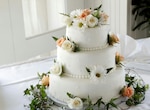 White, three-tiered wedding cake with white and pink flowers and greenery.