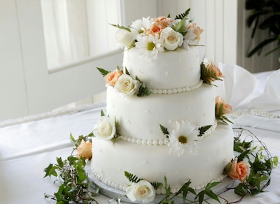 White, three-tiered wedding cake with white and pink flowers and greenery.