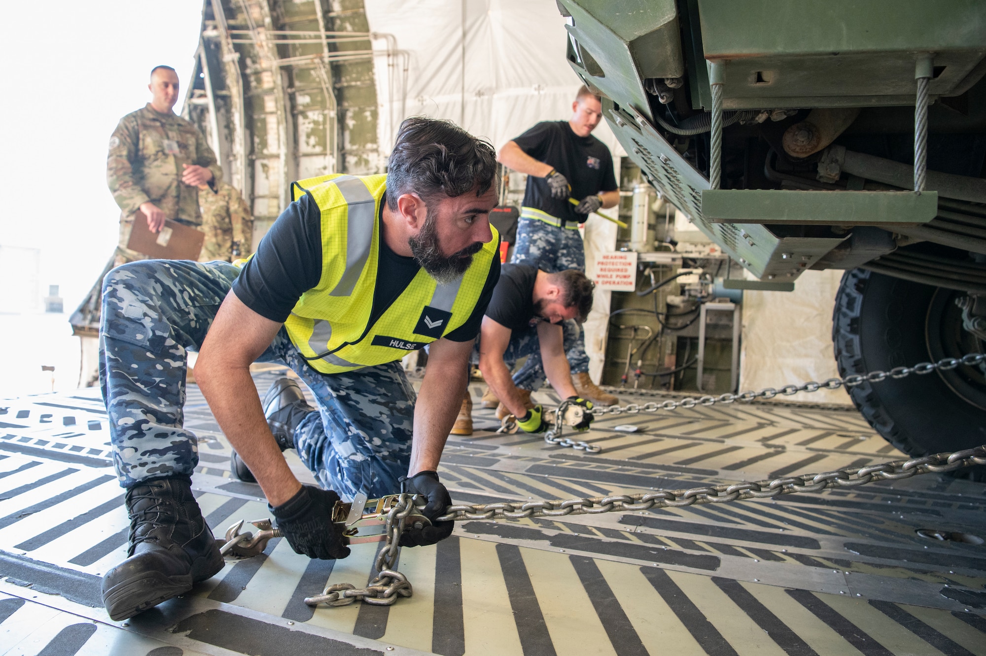 people in blue military uniforms load cargo onto an open aircraft ramp