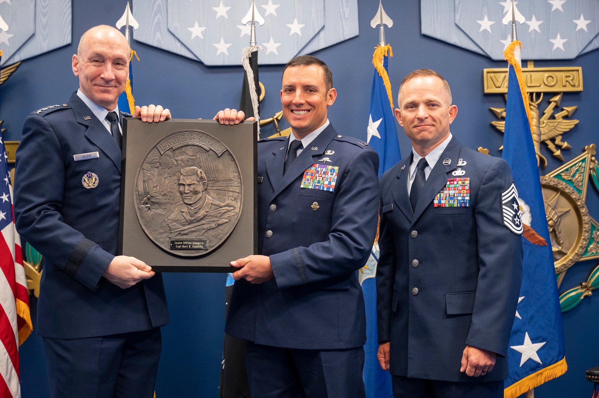 A man hands a plaque to another, the two alongside another man on the right pose for a portrait