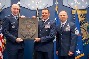 A man hands a plaque to another, the two alongside another man on the right pose for a portrait