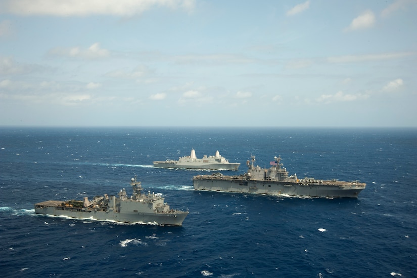 Three ships are in formation in the ocean going from left to right of frame.