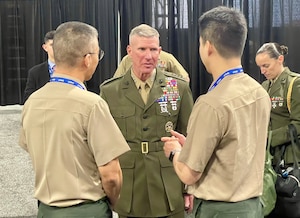 A man in a dress military uniform is talking to two men in uniforms with their backs to the camera.