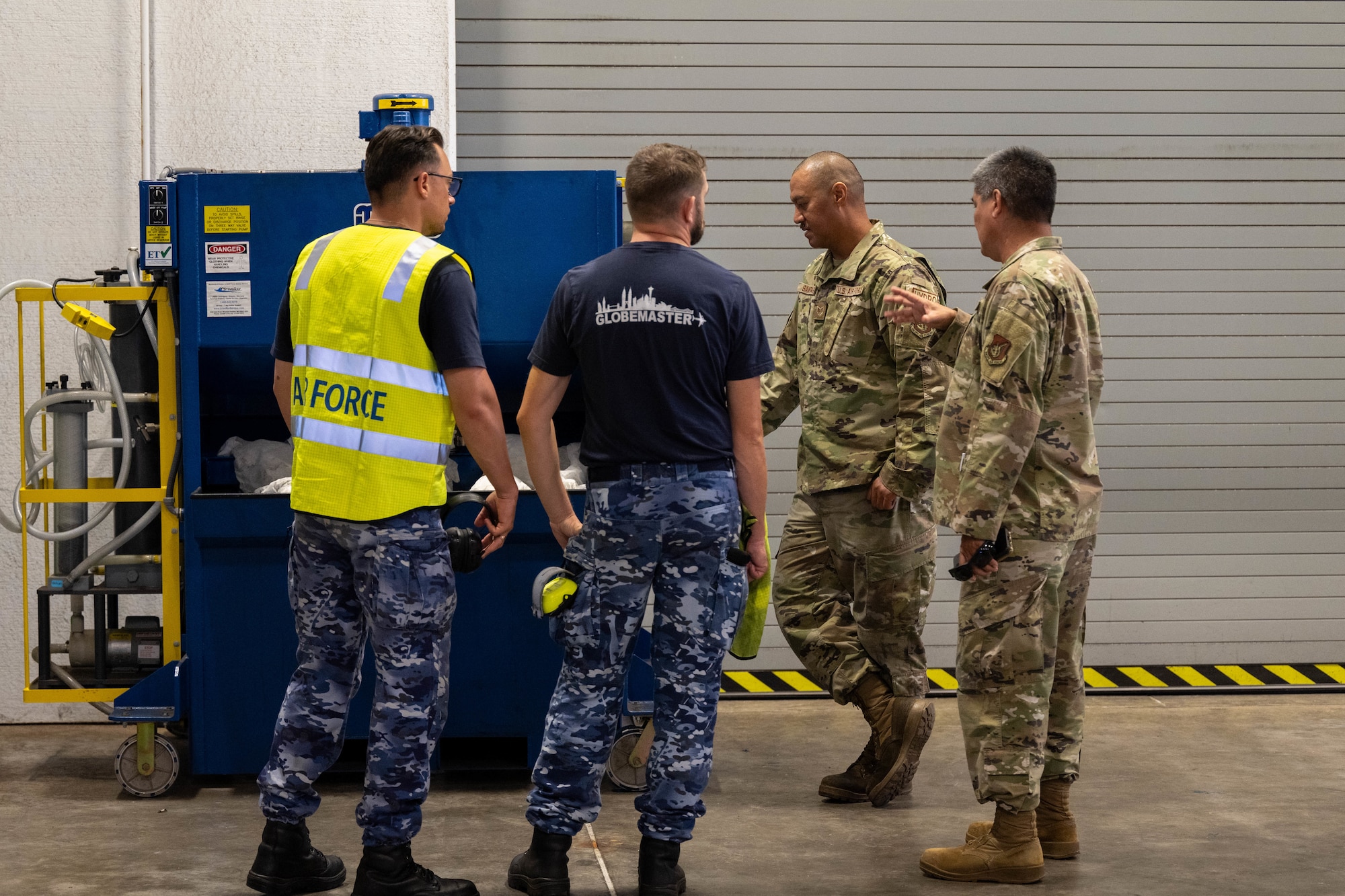 Two Royal Australian Air Force members talk to two U.S. Airmen about a Machine during a tour of the facility on Joint Base Pearl Harbor Hickam.