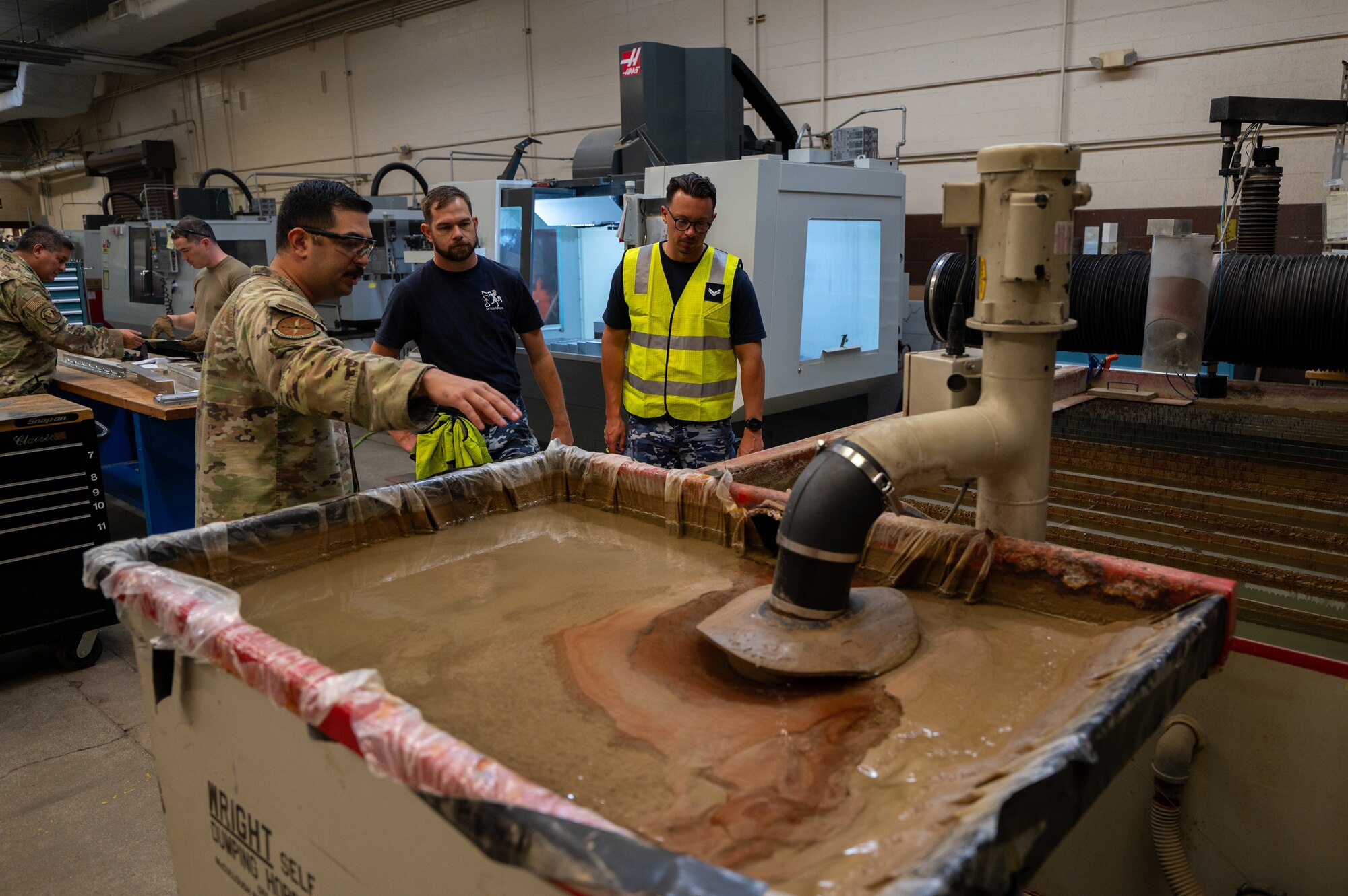 Airmen shows two Royal Australian Air Force members a large tank that cuts metal for aircraft piece.