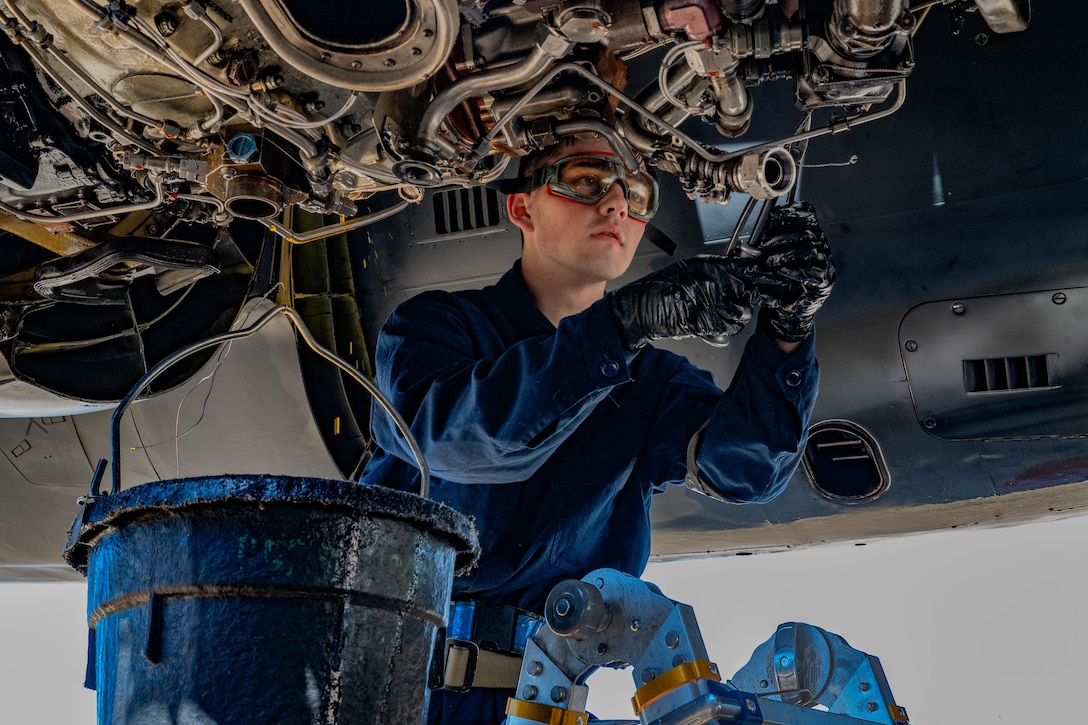 An airman wearing goggles focuses while performing maintenance on an aircraft.