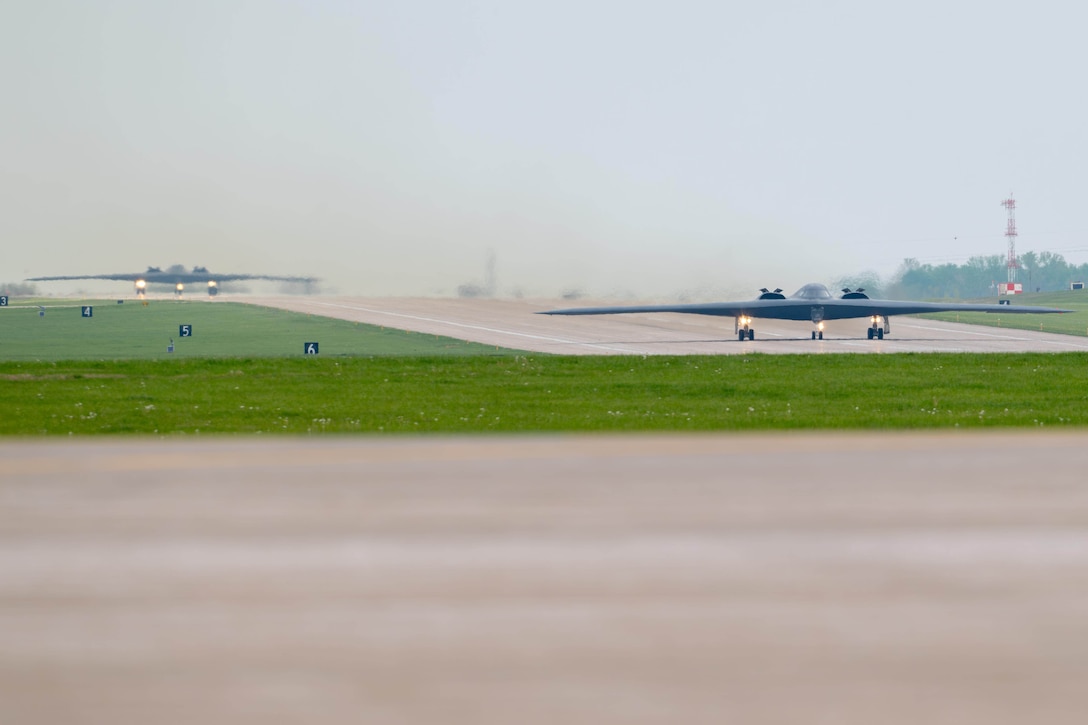 Two B-2 bombers taxi on a runway on a misty day.