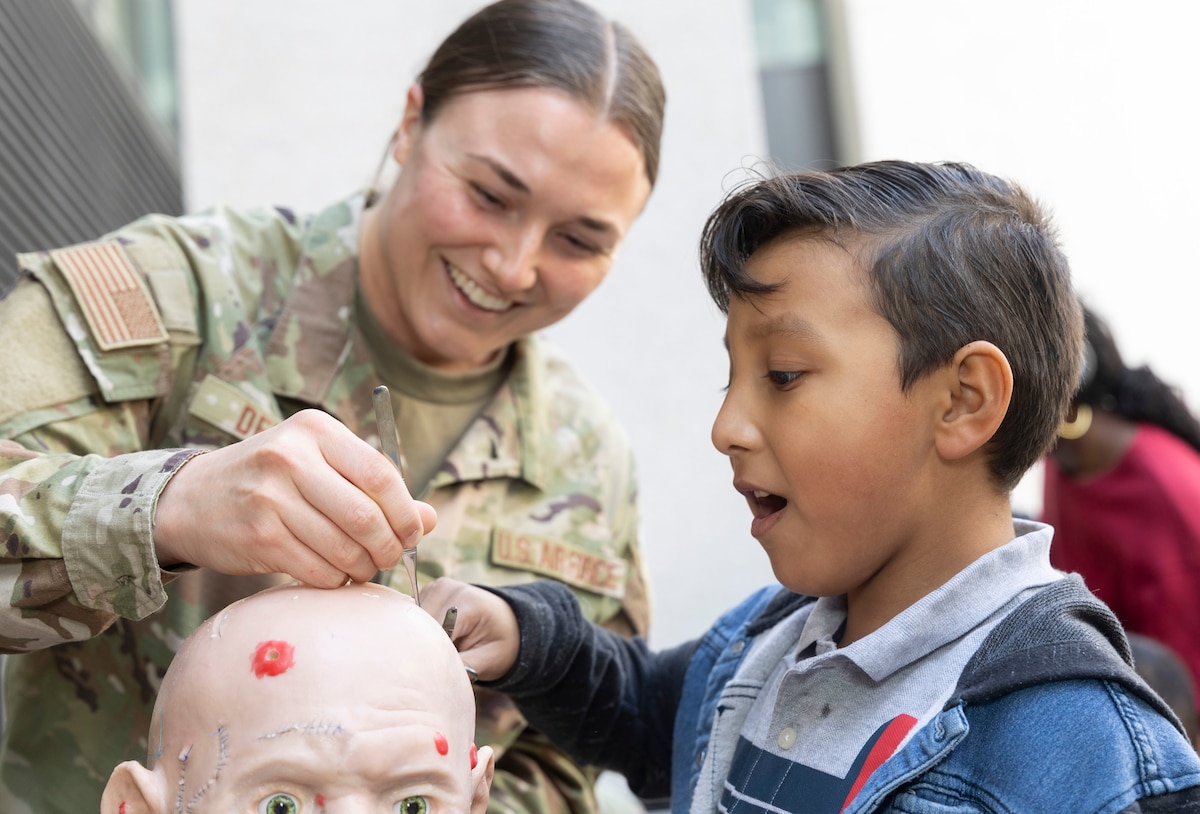 An airman guides a child through the process of removing sutures from a mannequin during a demonstration.