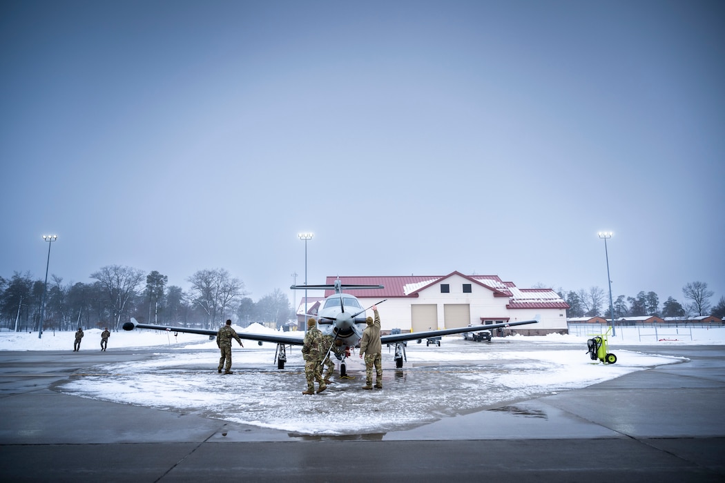 Aircrew inspect propeller plane on a foggy, snowy flight line.