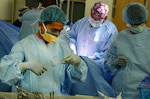 A surgical team wearing masks uses equipment in an operating room.