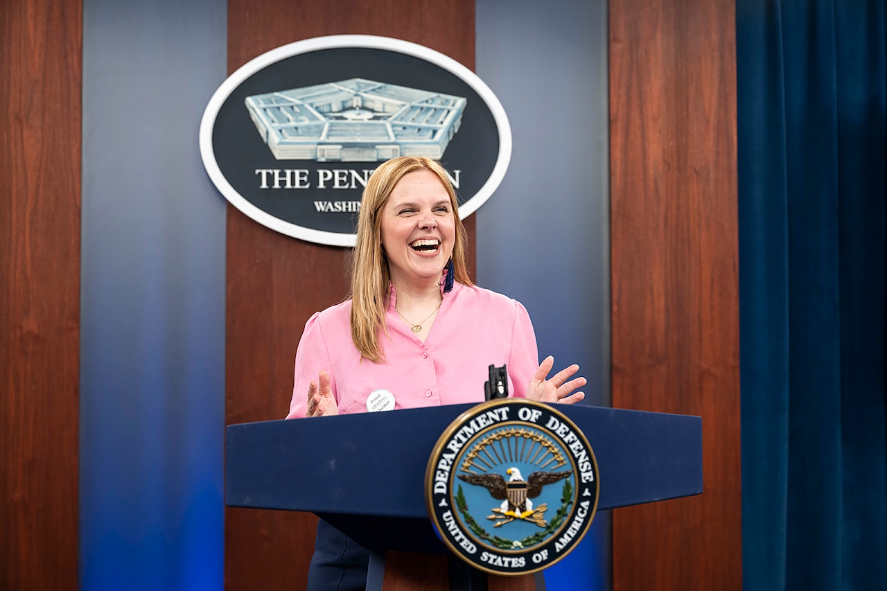 A civilian stands at a lectern adorned with the Defense Department seal.