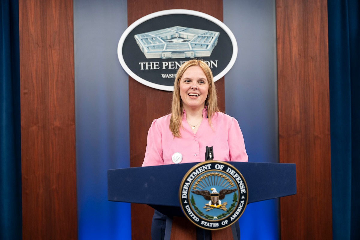 A civilian stands at a lectern adorned with the Defense Department seal.