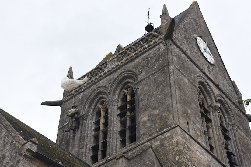A mannequin hangs from a church steeple.